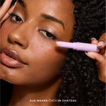 Woman applying makeup with a purple eyeshadow labeled 'GoGo' on a neutral background [Chateau]