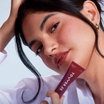 A close up of a model holding Tower 28 Beauty's LipSoftie™ Lip Treatment in Ube Vanilla and wearing it on her lips. [Ube Vanilla]