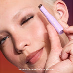 Close-up of a person applying makeup with a purple pen, featuring the brand on the product. [Whisky]