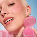 A person holds Tower 28 Beauty’s GetSet Powder Blush in the shade Malibu Cooler with a swatch of cool baby pink on their cheek. [Malibu Cooler]