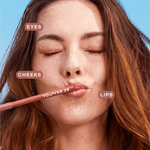 A person wearing the Tower 28 Beauty OneLiner in the shade Paint My Number on her lips, cheeks, and eyes. [Paint My Number]