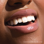 Oat [Closeup photo of very glossy lips, smiling and wearing the Tower 28 Beauty ShineOn Milky Lip Jelly shade in Oat (a milky peachy-pink)]